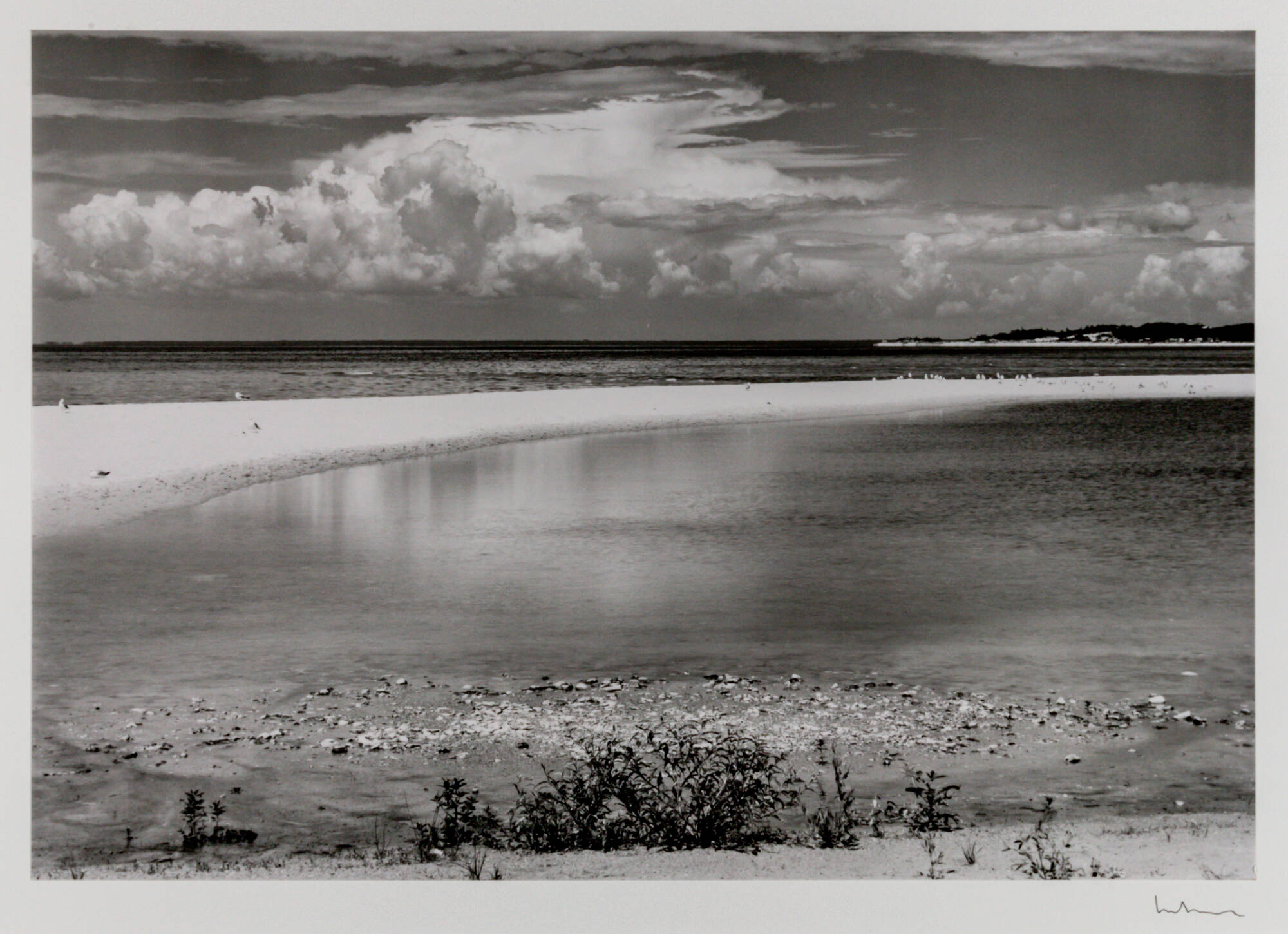 Black and white photograph landscape of a thin line of sand surrounded by water, clouds in the sky.
